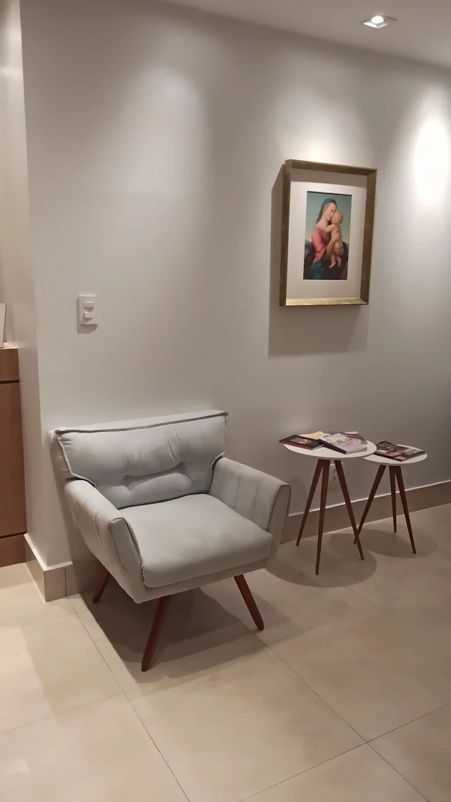 Sala de espera com poltrona cinza, mesa lateral e um quadro na parede