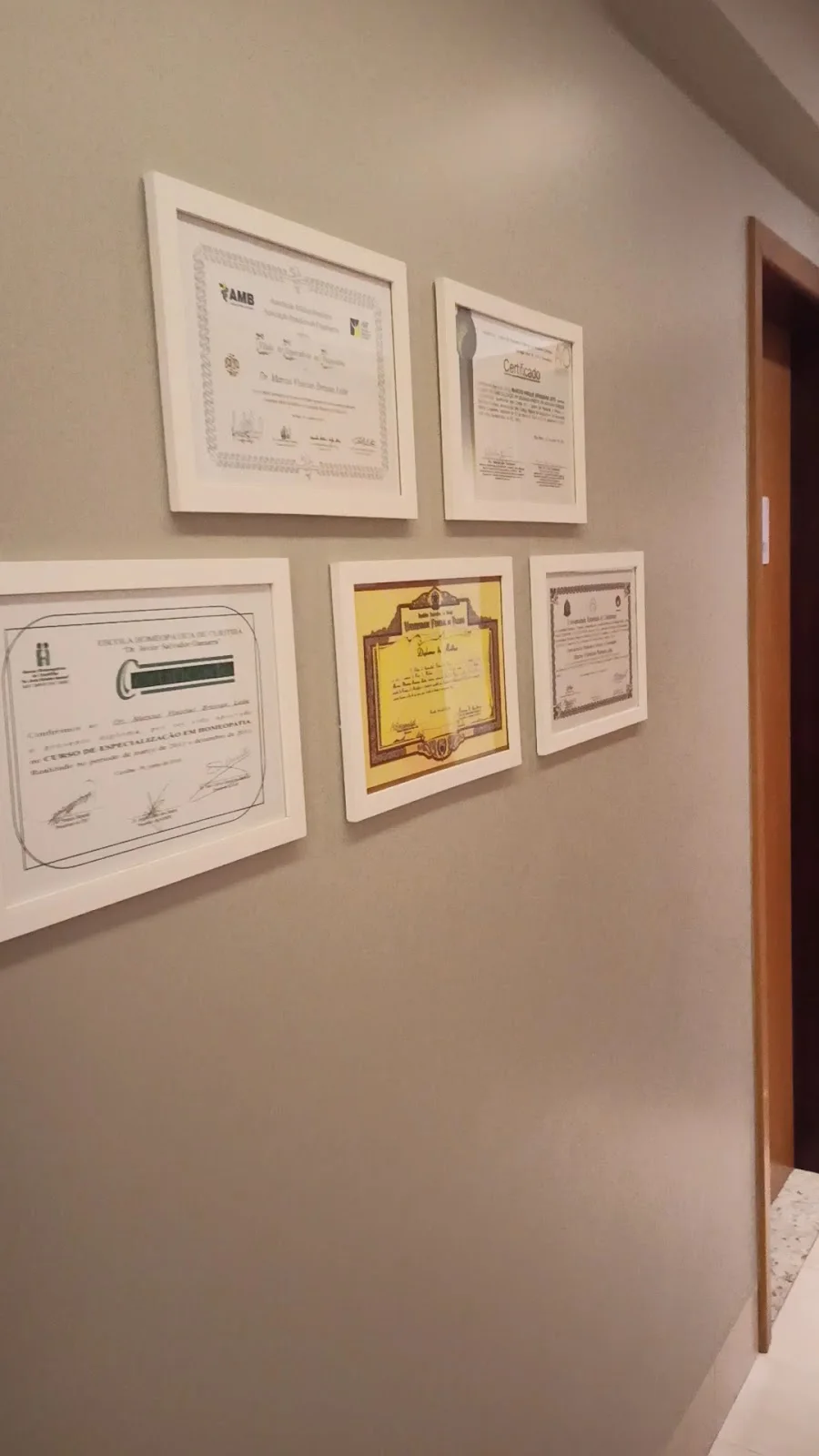 A parede do corredor da Clínica Avicena com os diplomas emoldurados