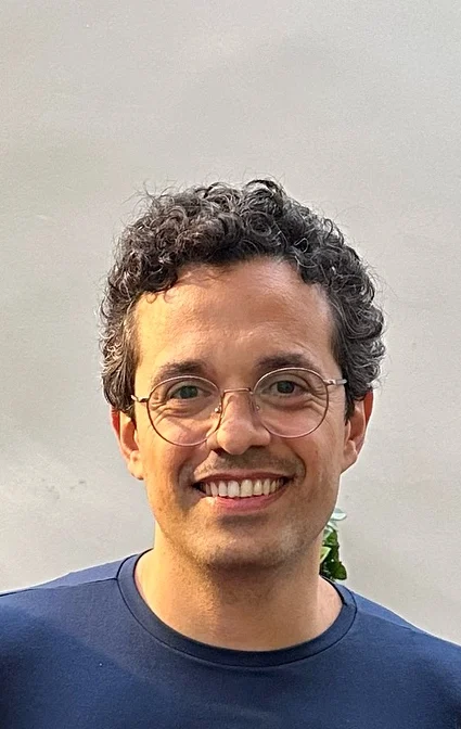 Dr. Marcus Bressan, de óculos redondos e camiseta azul-marinho, sorrindo ao ar livre